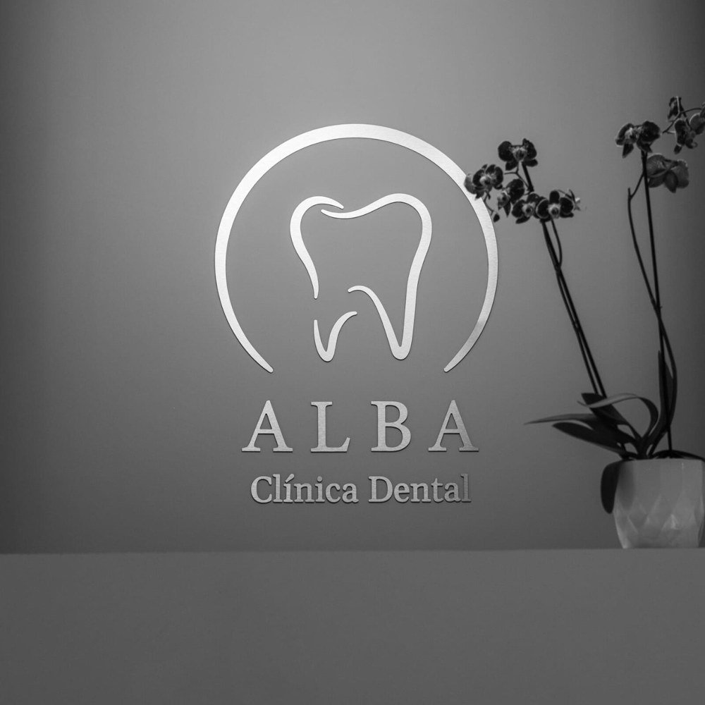 Logotipo de Alba Clínica Dental en pared gris con iluminación moderna en la recepción.
